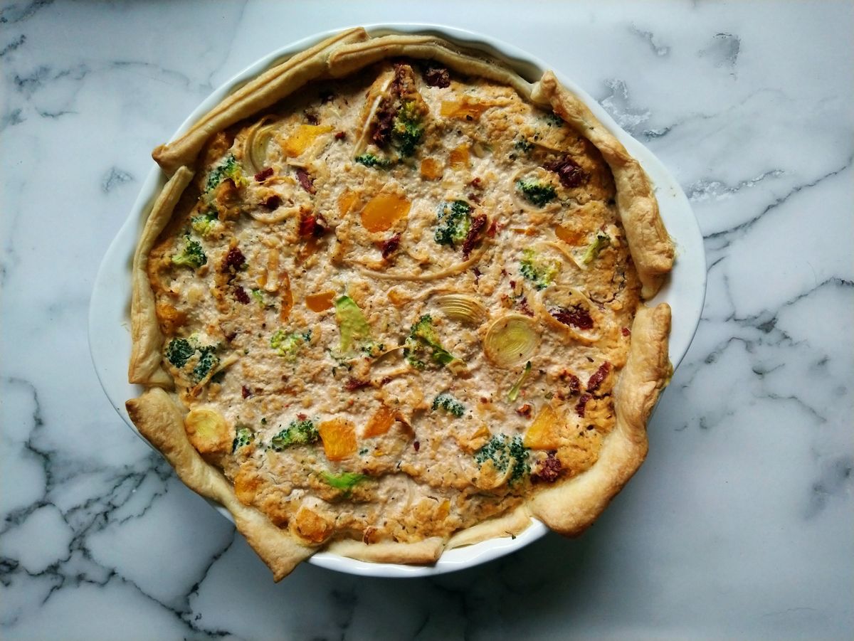 Rustic vegetable quiche with broccoli, orange squash cubes and leek in a white pie dish