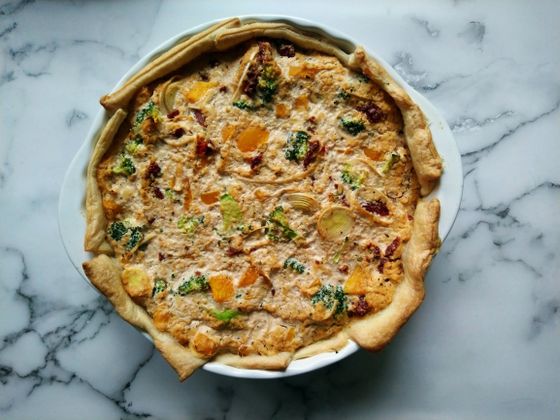 Rustic vegetable quiche with broccoli, orange squash cubes and leek in a white pie dish