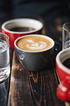 Close-up of latte art with cups of coffee and water on a rustic wooden table.