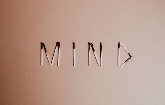 Creative still life of burnt matchsticks spelling 'Mind' on a textured beige surface.