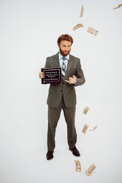 Free Confident businessman in a suit holding an award plaque with cash floating around. Stock Photo