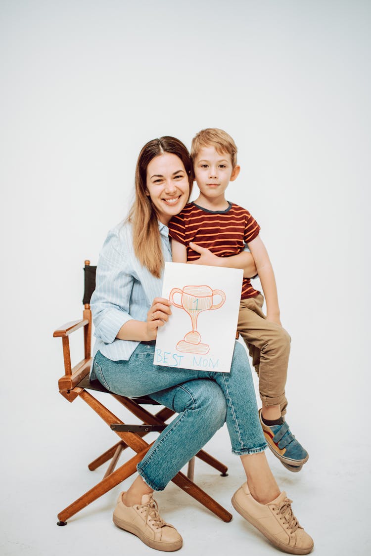 A Boy Sitting On A Woman Holding A Trophy Drawing On Paper 