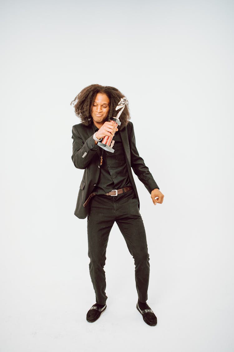 Man In Black Suit Dancing With A Trophy On Hand