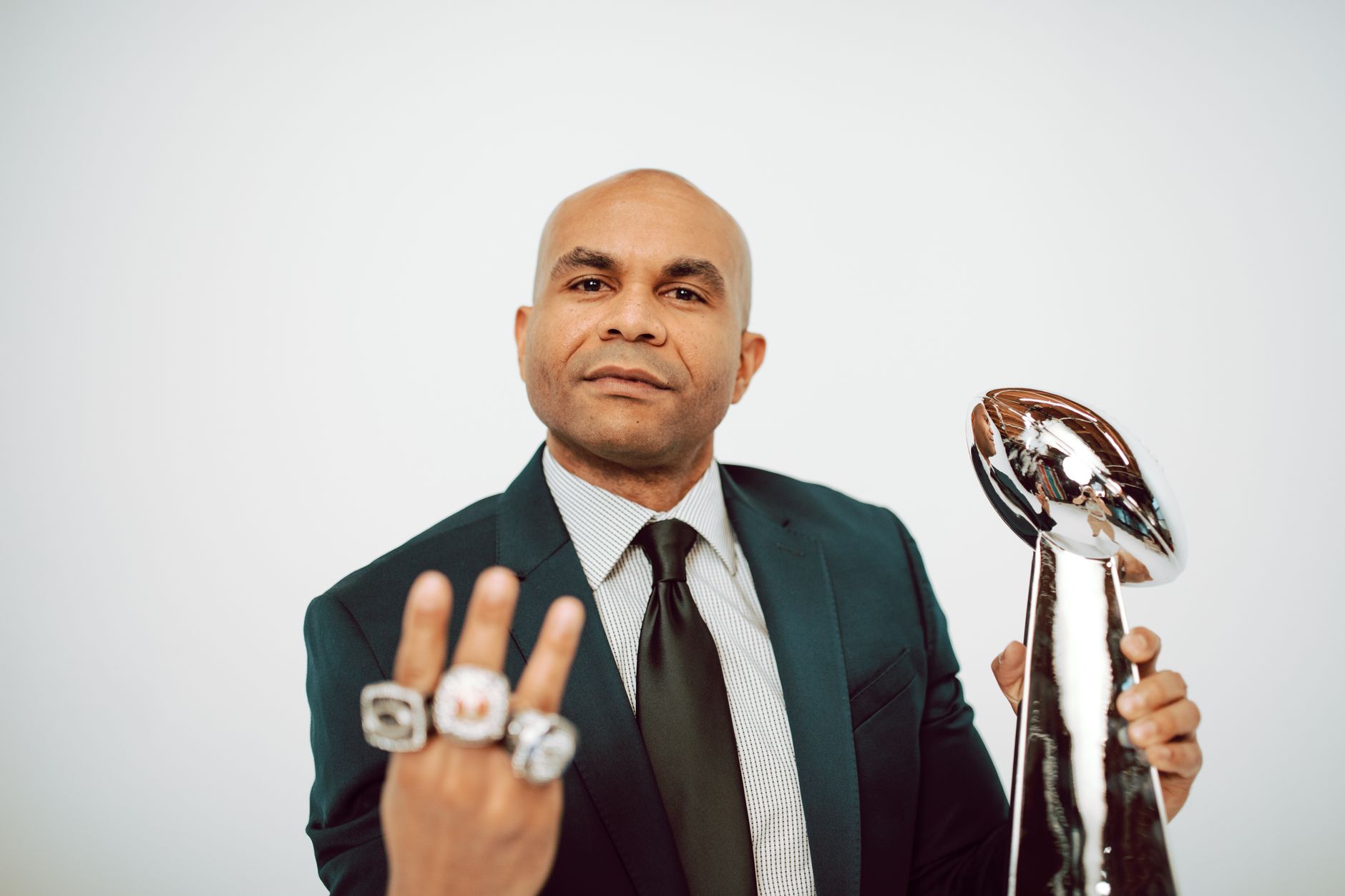 Confident man in a suit showcasing victory rings and trophy on a white background.