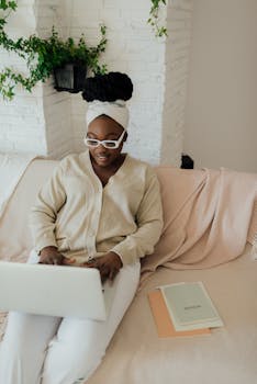 A black woman using a laptop on a couch, working from home in a cozy setting.