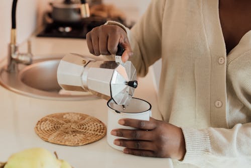 A Person Holding a Stainless Teapot Over a Mug