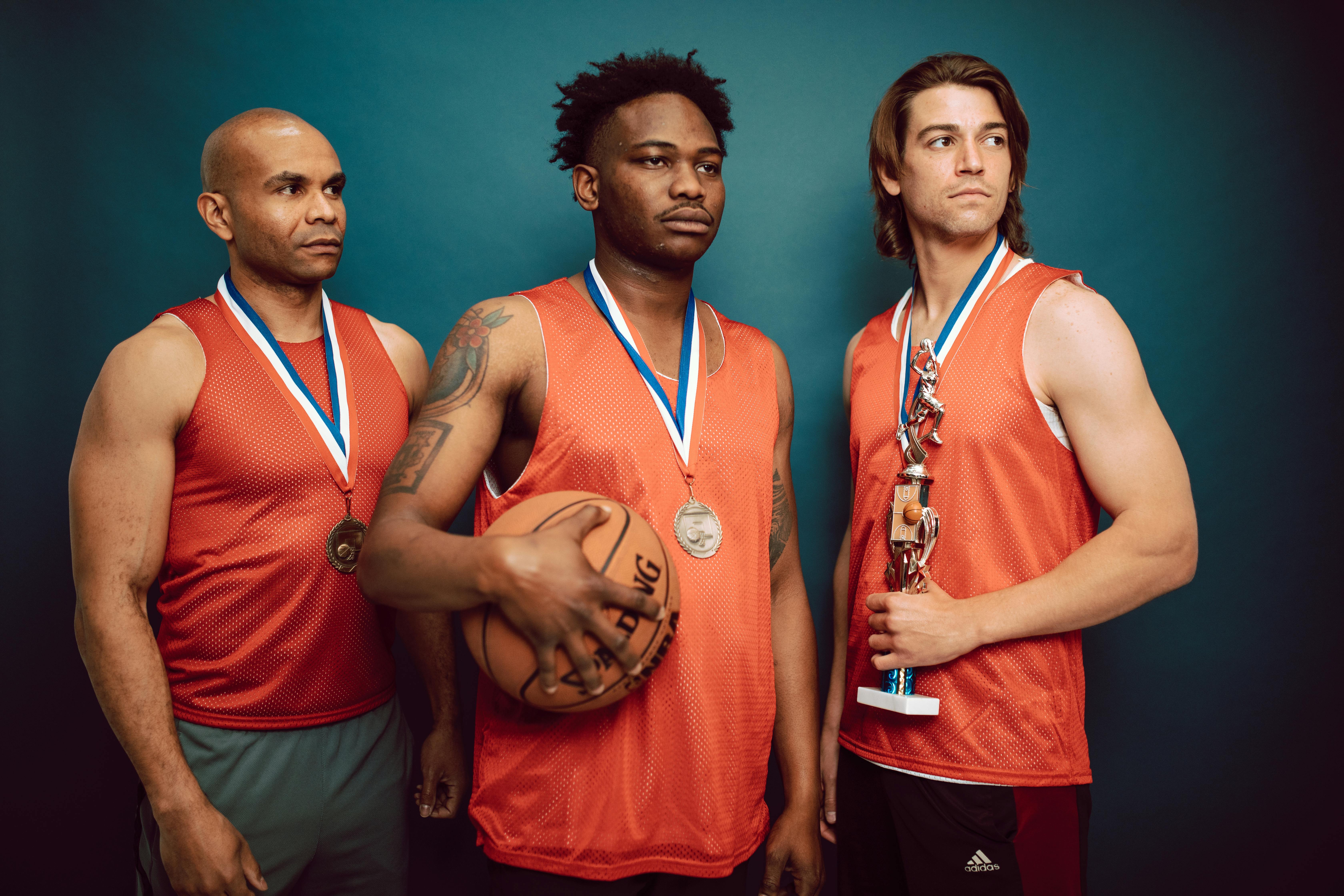 three men wearing medals in orange jersey holding a basketball and trophy