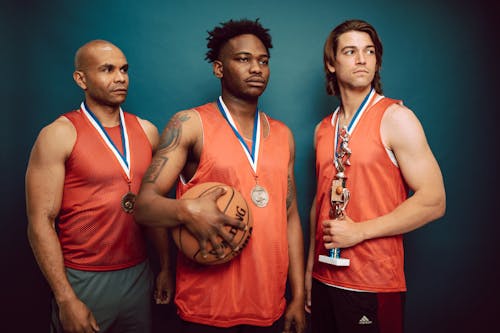 Three Men Wearing Medals in Orange Jersey Holding a Basketball and Trophy