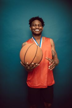 Happy male basketball player smiling while holding a ball in the studio.