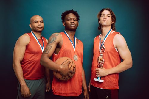 Free Three basketball players posing confidently with medals and a trophy in a studio. Stock Photo