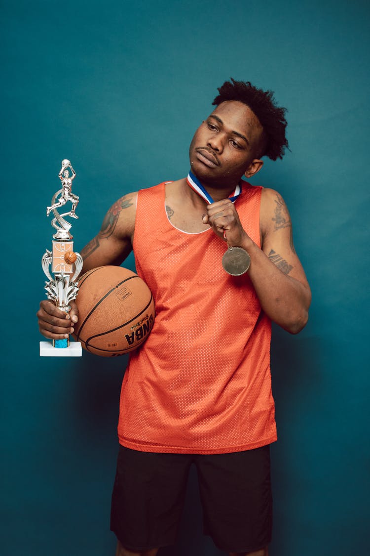 A Basketball Player Posing With A Medal And A Trophy