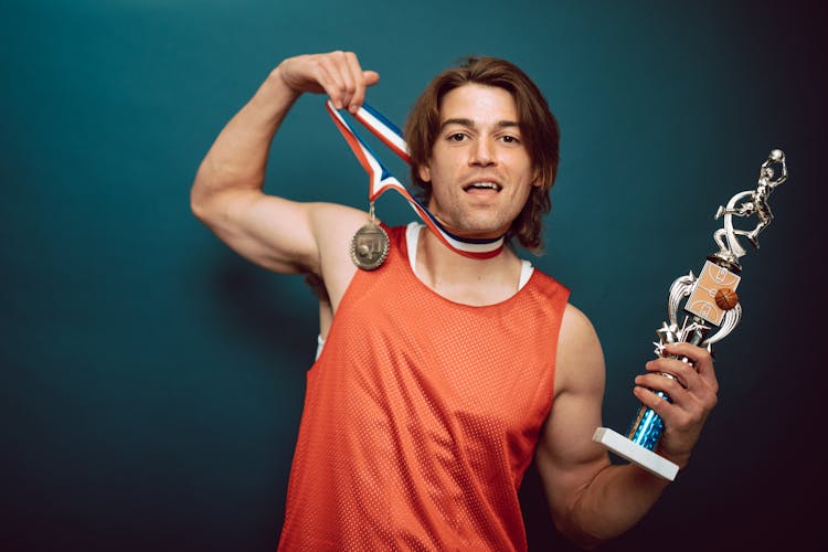 A Basketball Player Posing With A Medal And A Trophy