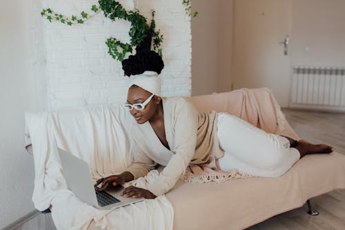 Free Woman in White Framed Eyeglasses Lying on Couch Using Laptop Stock Photo