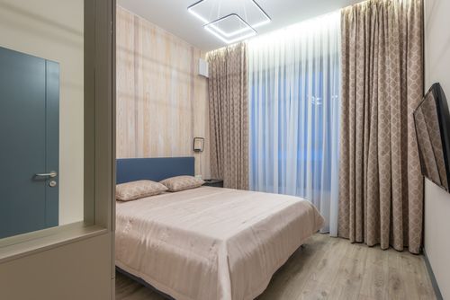 Free Comfortable bed with cushions and TV hanging on wall in cozy bedroom decorated with curtains Stock Photo