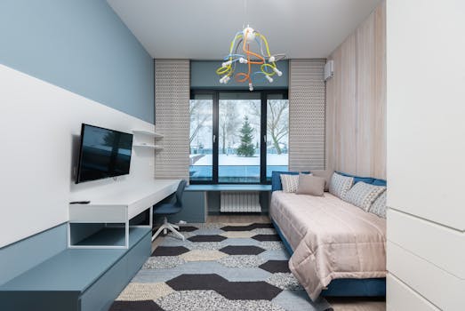 Interior of modern bedroom with comfortable sofa with cushions placed near wardrobe in front of working desk and TV