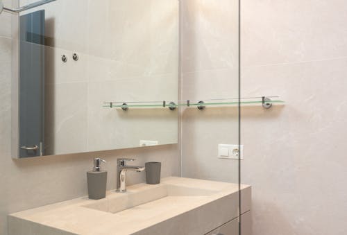 Through glass of shower cabin on sink and mirror in modern bathroom with tiled walls