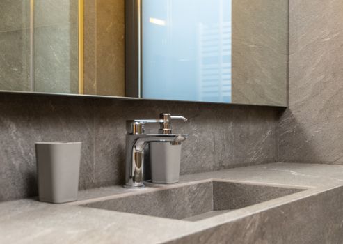 Chrome faucet and marble sink under mirror in modern bathroom with tiled walls