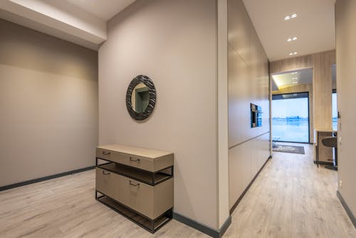 Round mirror and cabinet in spacious hallway of modern house with wooden parquet floor and panoramic windows