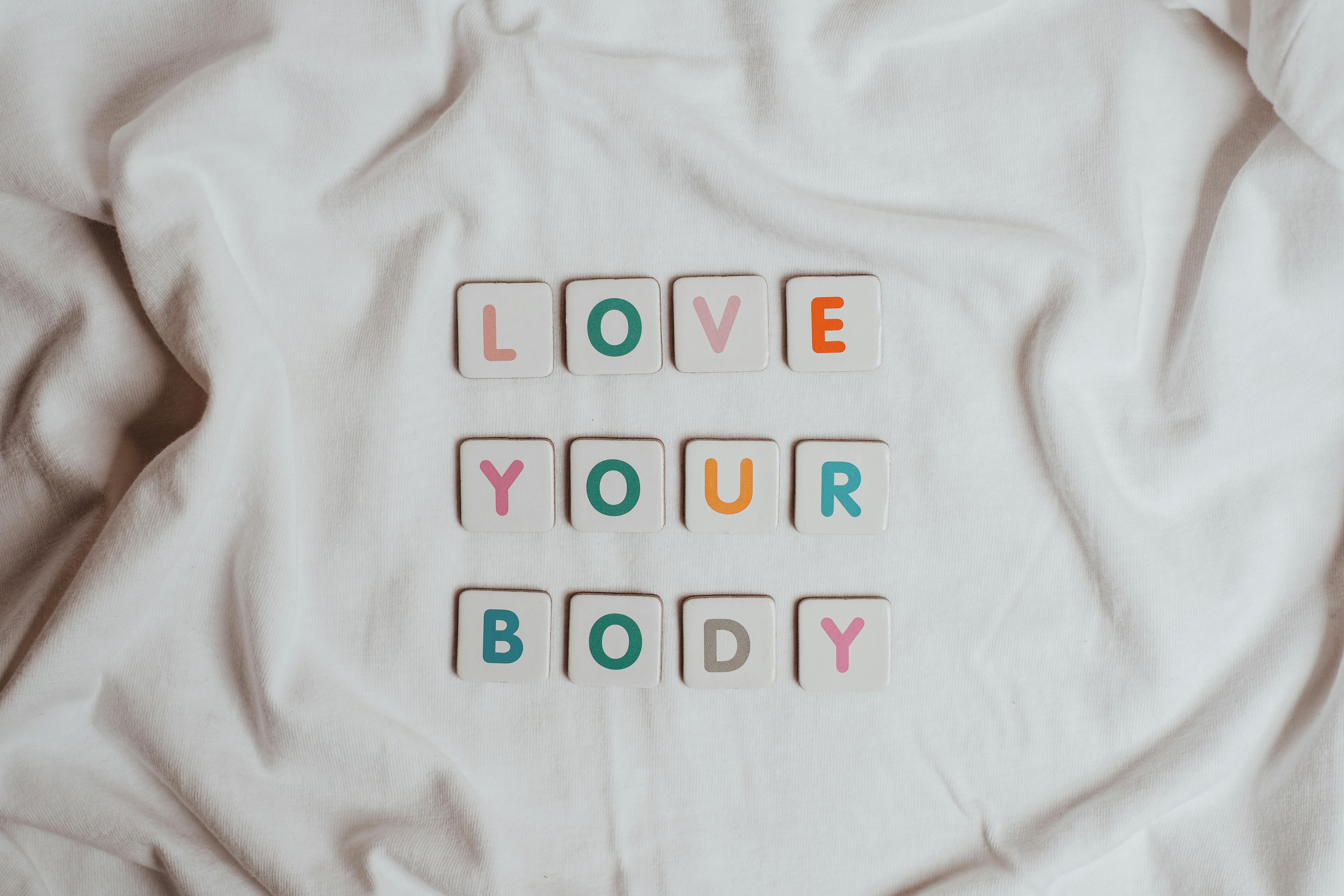 Inspiring 'Love Your Body' message displayed on a soft white fabric background.