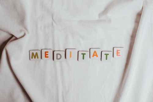 Free Colorful letter tiles spell 'meditate' on soft white fabric. Perfect for mindfulness themes. Stock Photo