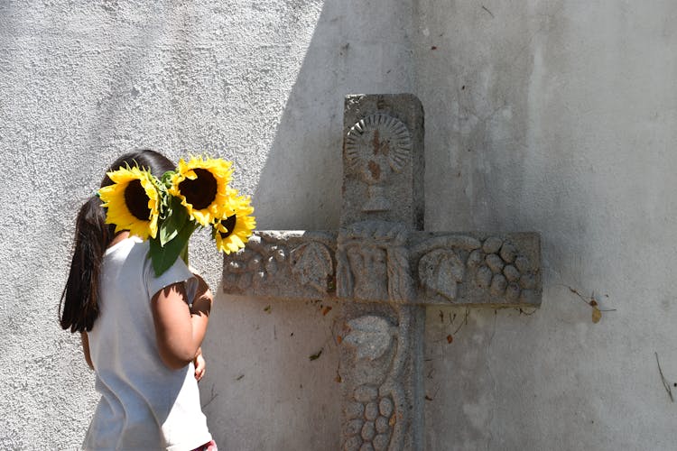 A Girl With Sunflowers Next To A Cross