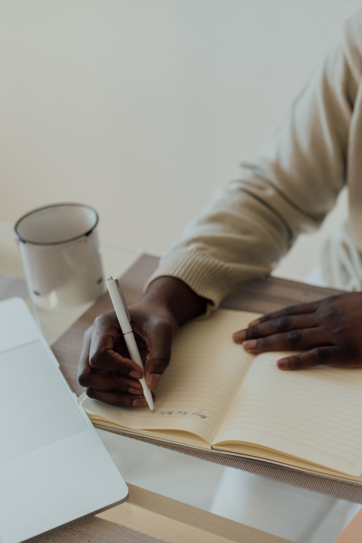 Hands writing in an open notebook at a table in warm morning light