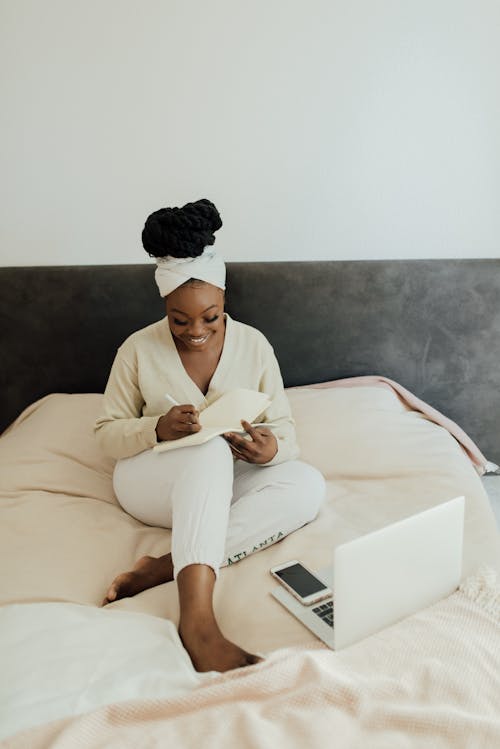 Free A Woman Writing on a Notebook while Sitting in Bed Stock Photo