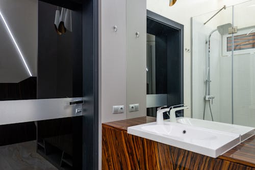 White ceramic sink with chrome faucet on wooden cabinet and shower cabin with glass walls in modern bathroom