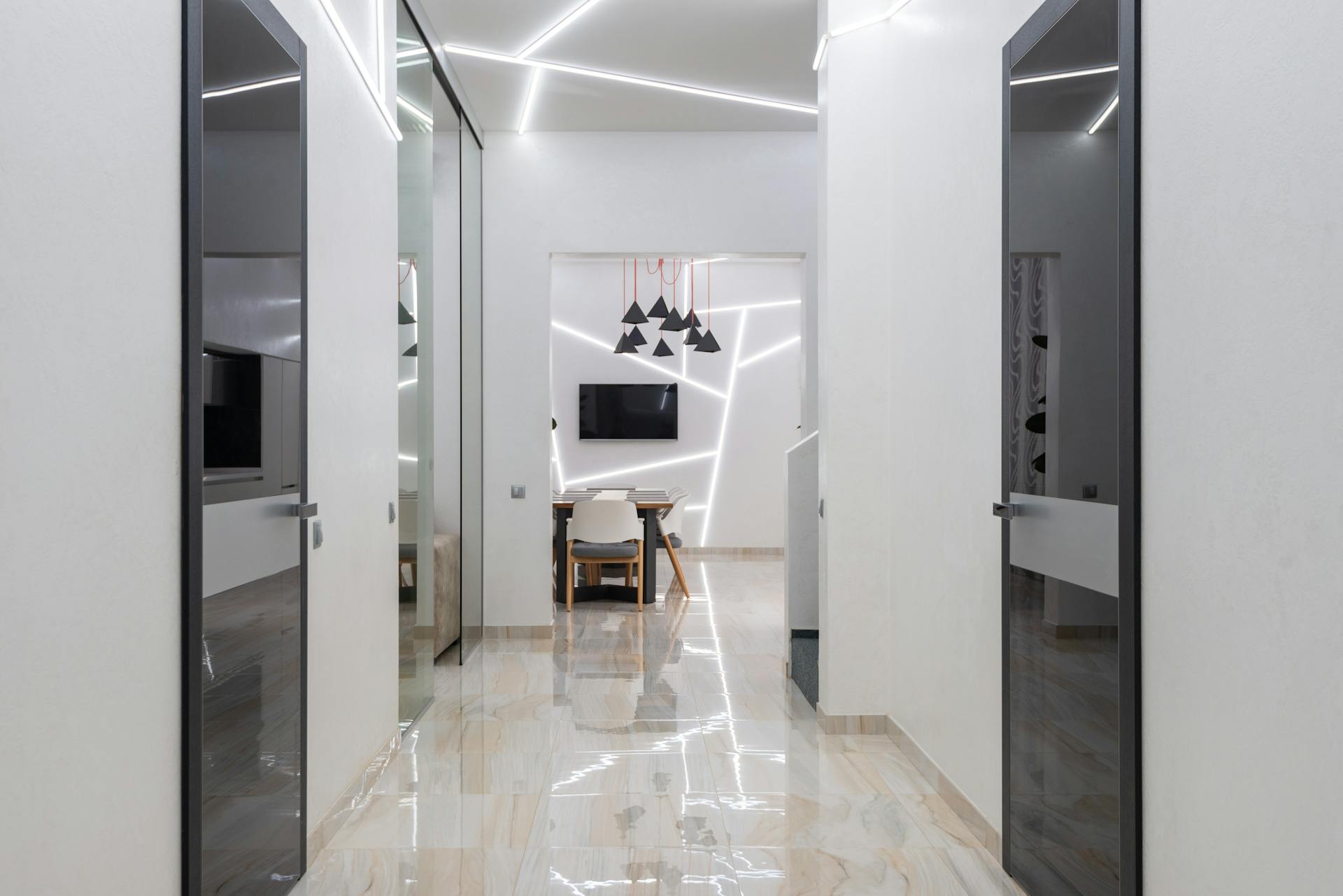 Interior of empty spacious hallway in house with glass doors and white walls near table with chairs next to TV under lamps