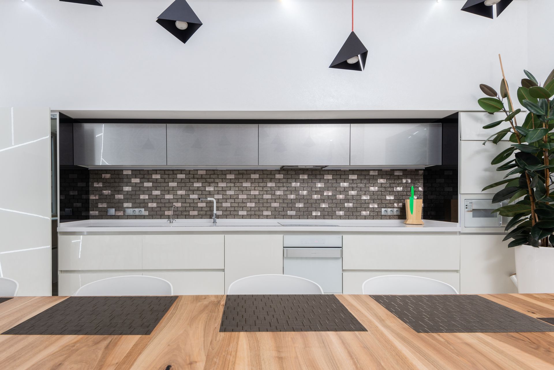 Interior of modern light kitchen with wooden table and chairs against modern minimalist white cabinets under geometric pendant lamps