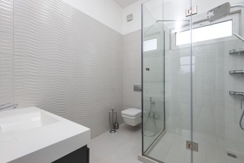 Free Shower room with glass walls against toilet bowl and washbasin above tiled floor in light house Stock Photo