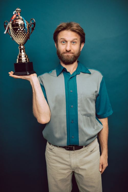 Free A bearded man confidently holds a trophy in a studio setting, showcasing victory and accomplishment. Stock Photo