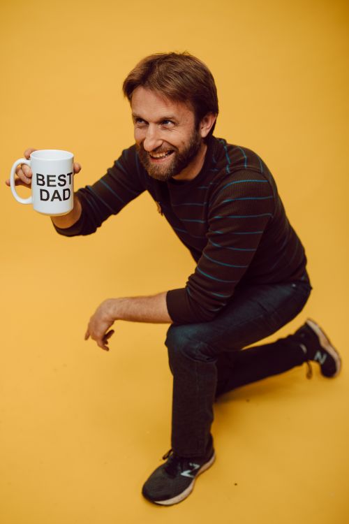 Free Smiling man kneeling on a yellow background holding a Best Dad mug. Stock Photo