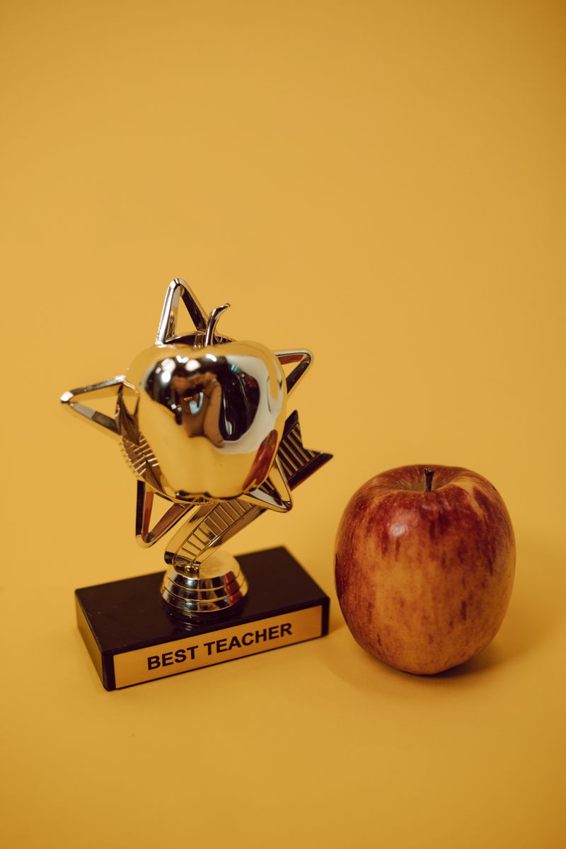 Award trophy and red apple set against a warm yellow backdrop symbolizing academic excellence.