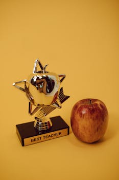Award trophy and red apple set against a warm yellow backdrop symbolizing academic excellence.