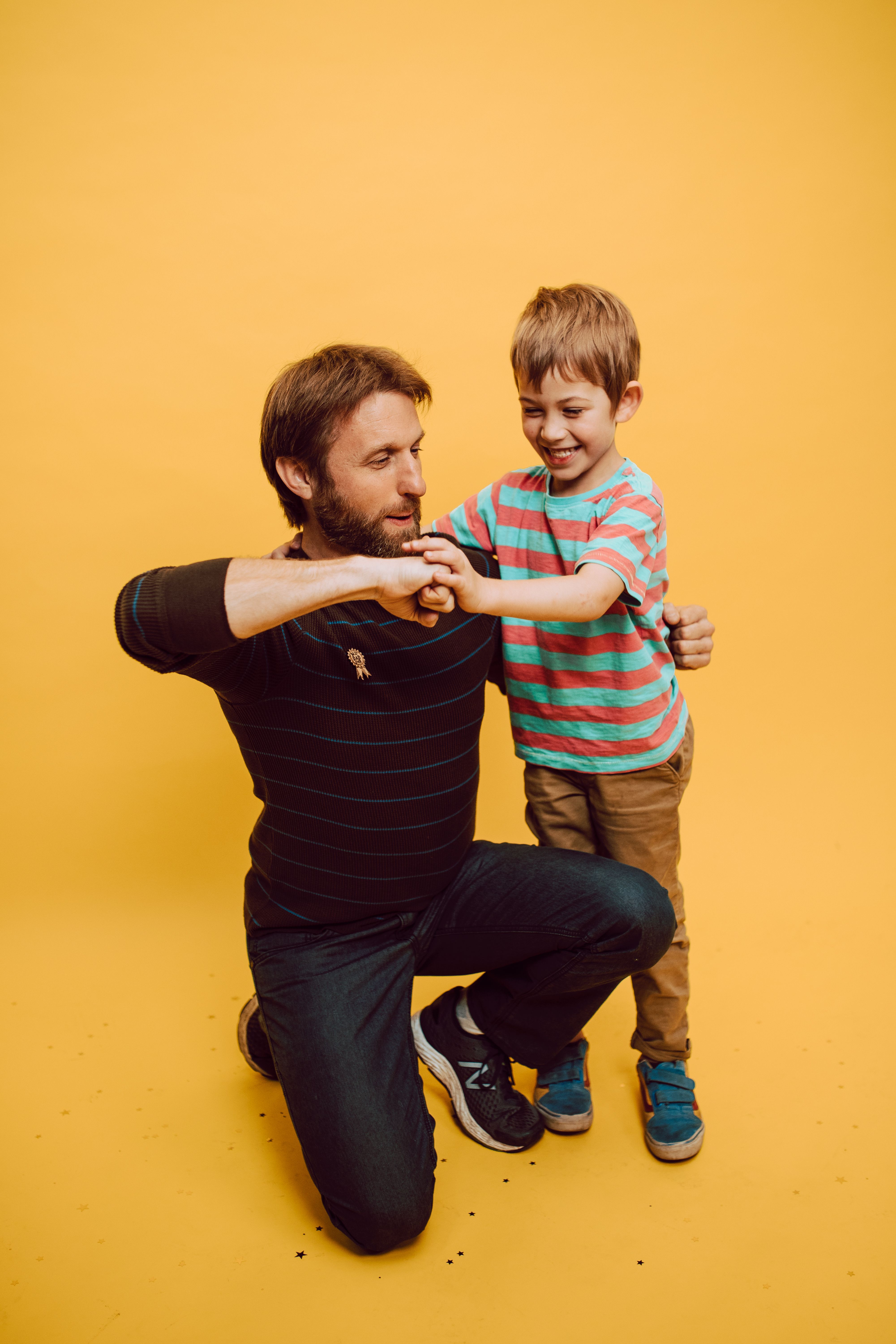 A happy father and son playfully fist bump against a vibrant yellow studio background.