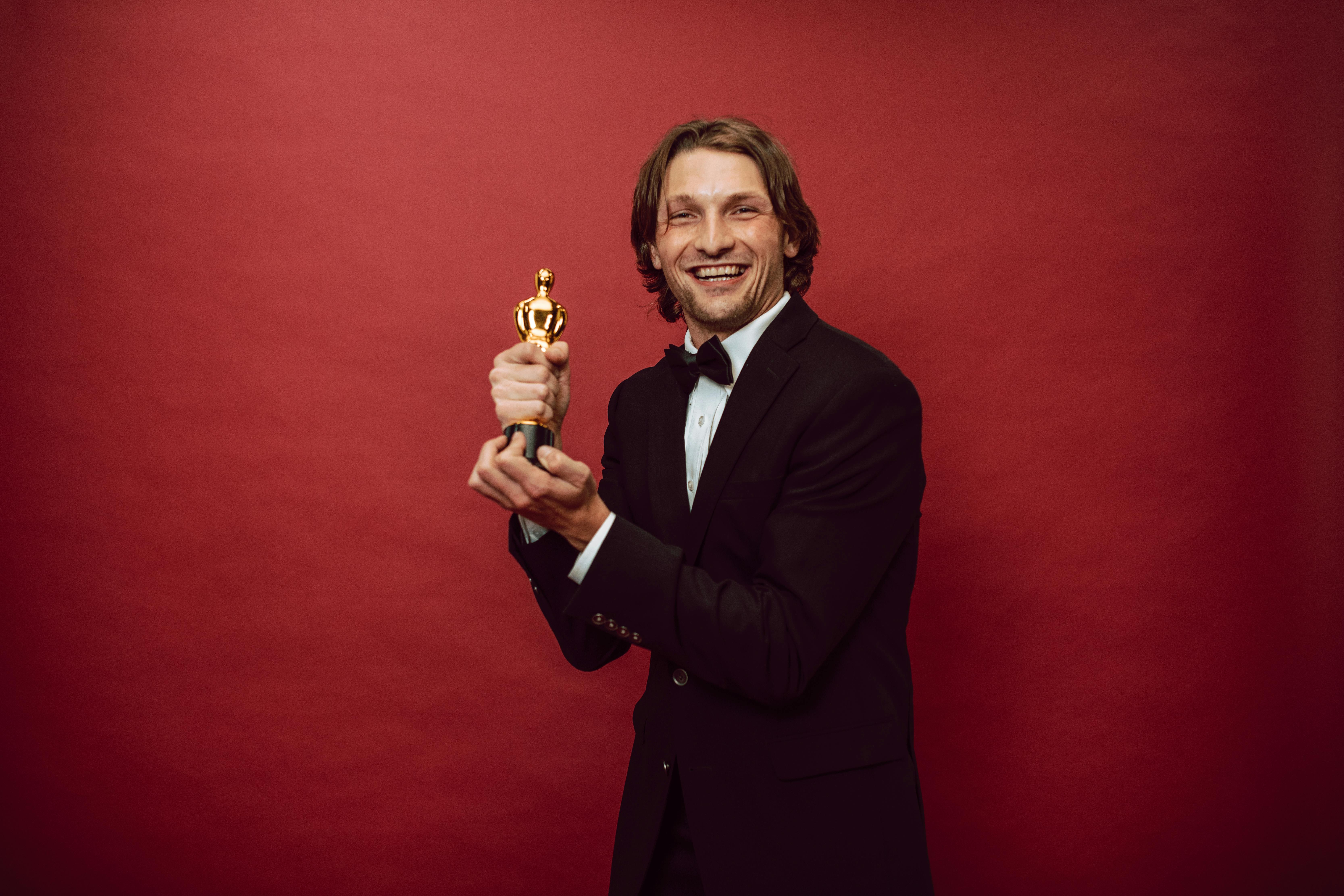 a happy man in a black suit holding his trophy