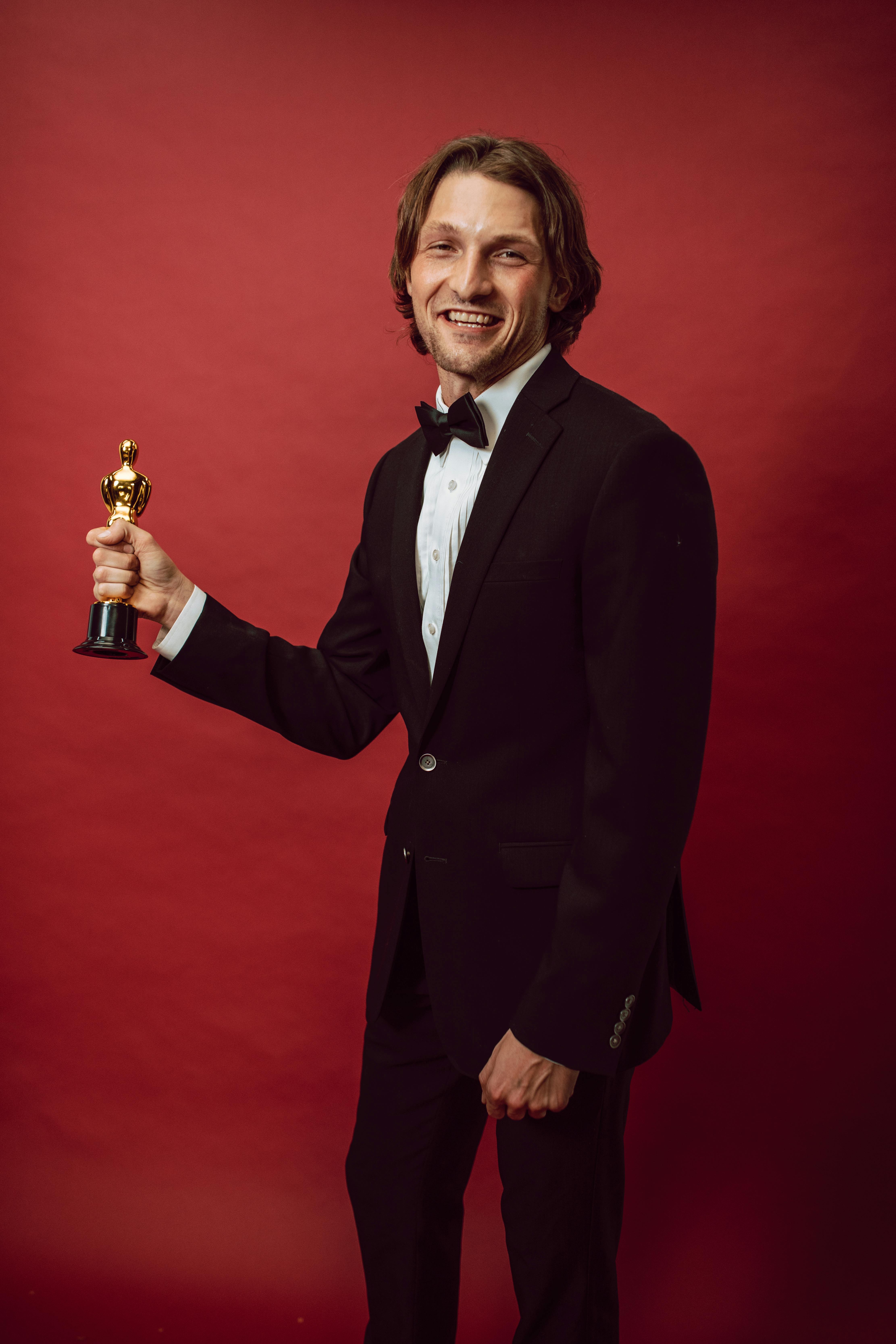 a man in a black suit holding a gold trophy