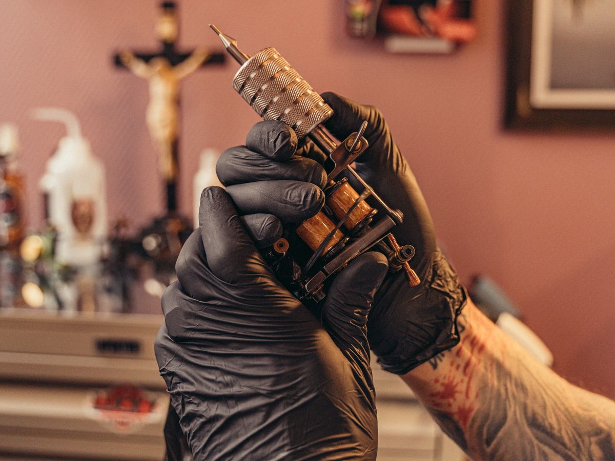 A tattoo artist checking a fresh piece in a hand mirror.