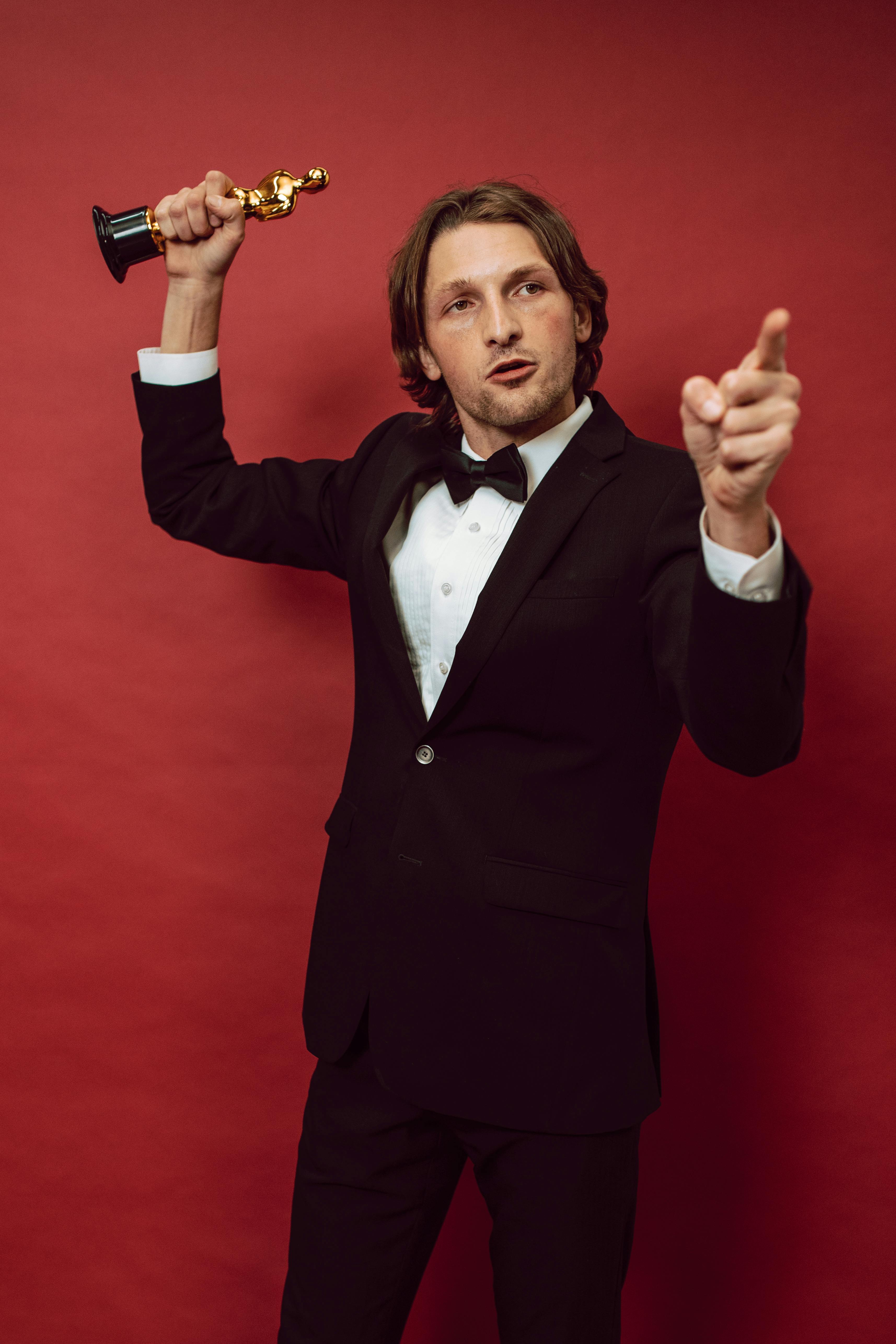 a man in a black suit holding a trophy and pointing with his finger