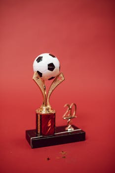 Elegant golden soccer trophy with red accents and soccer ball top on a red background.