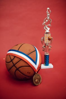 A basketball, trophy, and medal on a red backdrop symbolize sports success and achievement.