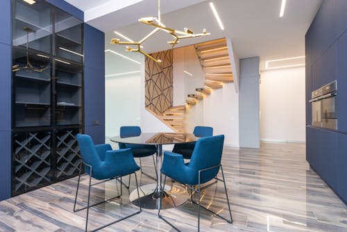 Armchairs and table against shelves on laminate under row of lamps in house with built in appliances