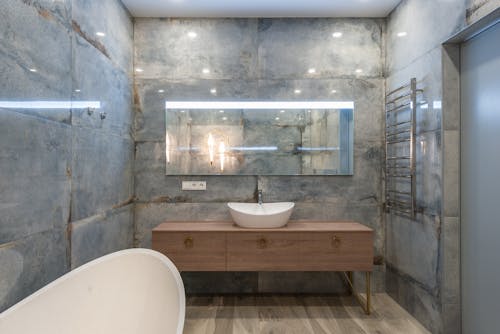 Creative design of bathroom with washstand on cabinet under mirror on stone wall against bathtub in house
