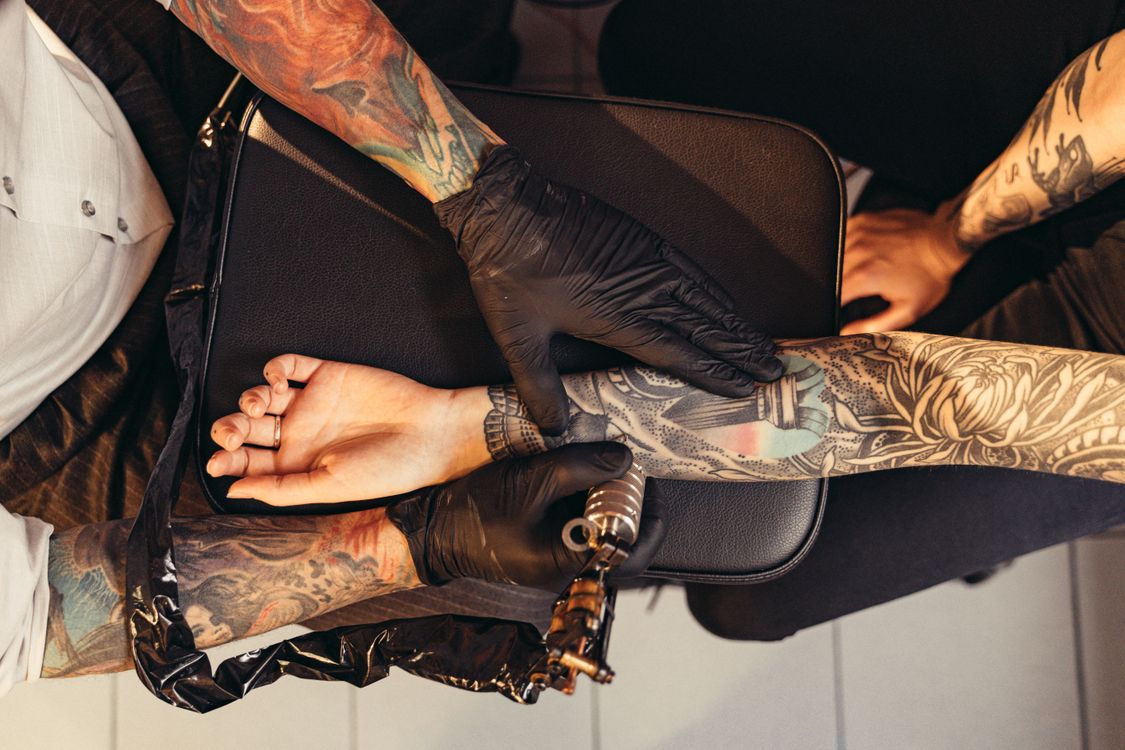 Overhead view of a tattoo artist working on a detailed sleeve tattoo on a client's arm in a professional studio