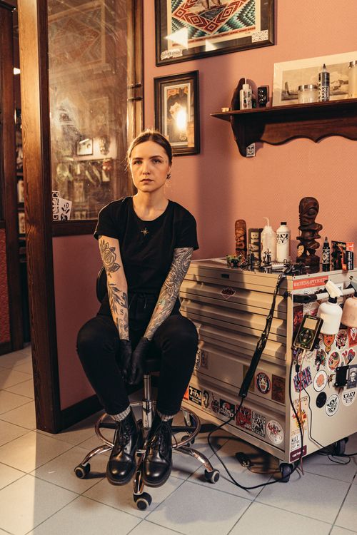 Free A female tattoo artist sitting in a tattoo parlor with tattoos visible on her arms, reflecting a modern and artistic vibe. Stock Photo