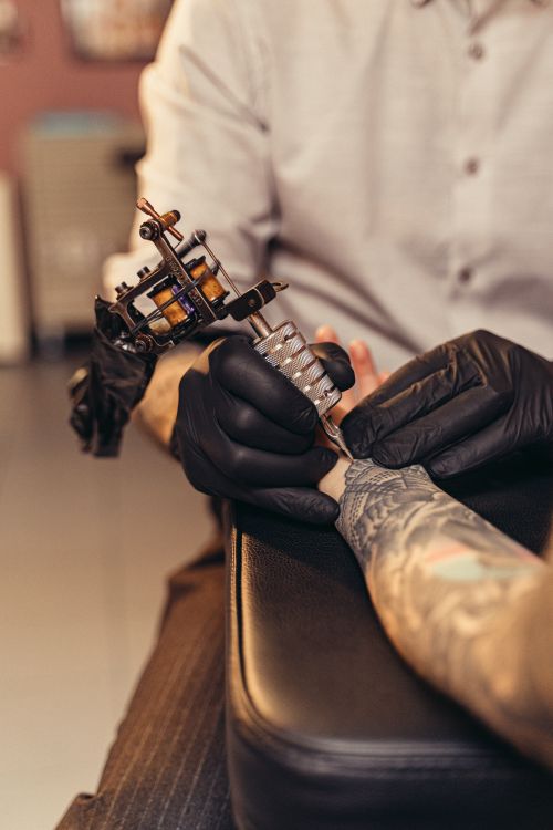 Free Tattoo artist working on client's arm in studio, highlighting intricate body art. Stock Photo