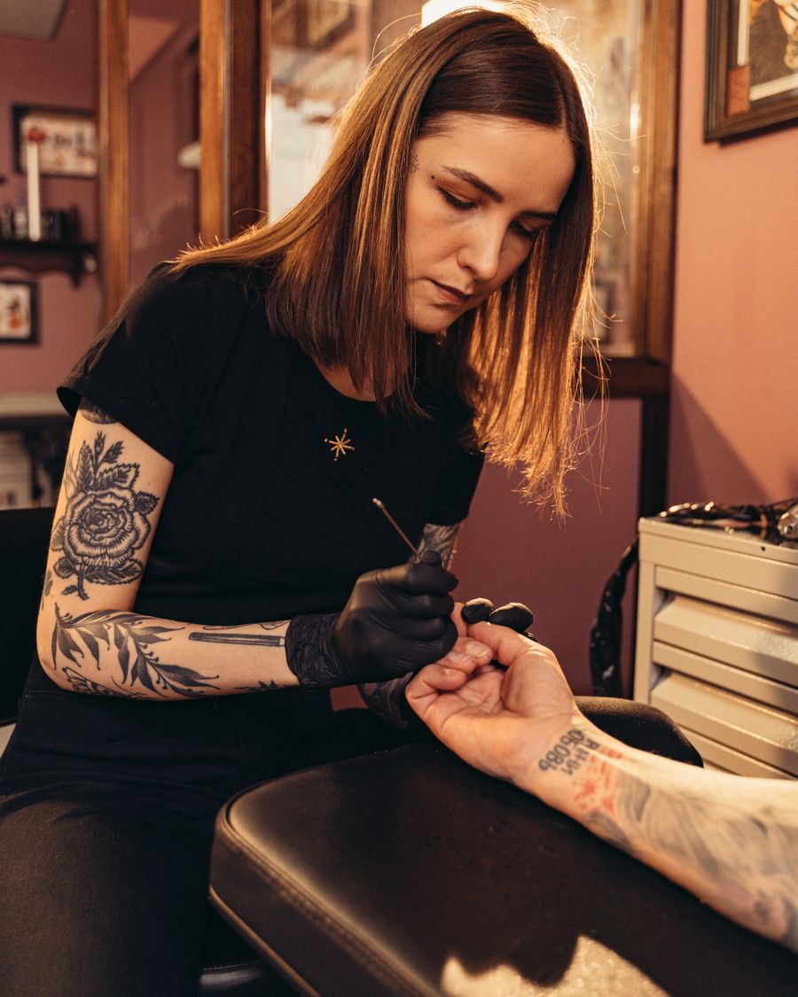 A female tattoo artist at work on a back piece at her station.