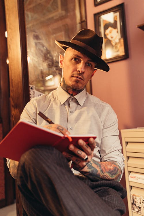 Free A Man in a Fedora Hat Holding a Pen and a Notebook Stock Photo