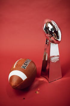Football and silver trophy on red backdrop symbolizing victory and achievement.